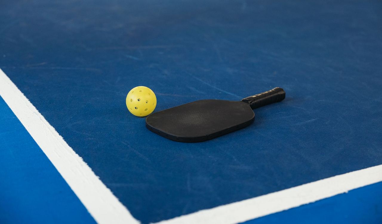 Black paddle and yellow ball on a blue court, illustrative equipment photograph