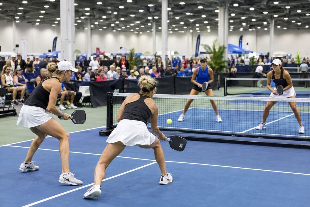 Professional pickleball players competing inside a large convention center venue with multiple courts and spectators