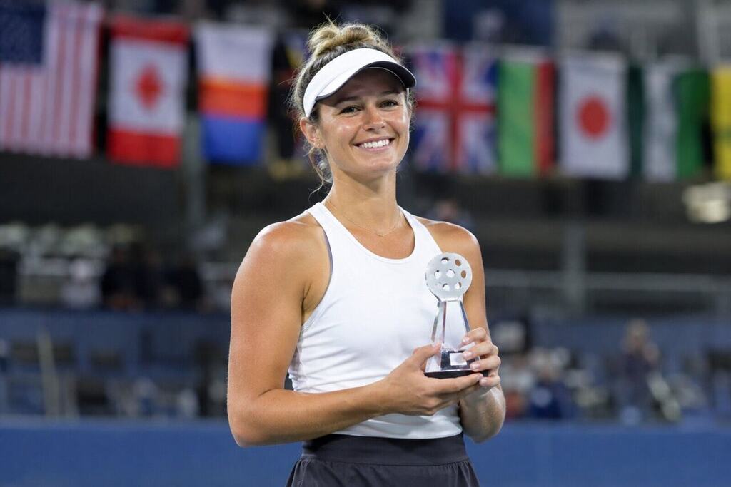 A female pickleball player holding a trophy and smiling with international flags visible in the arena background