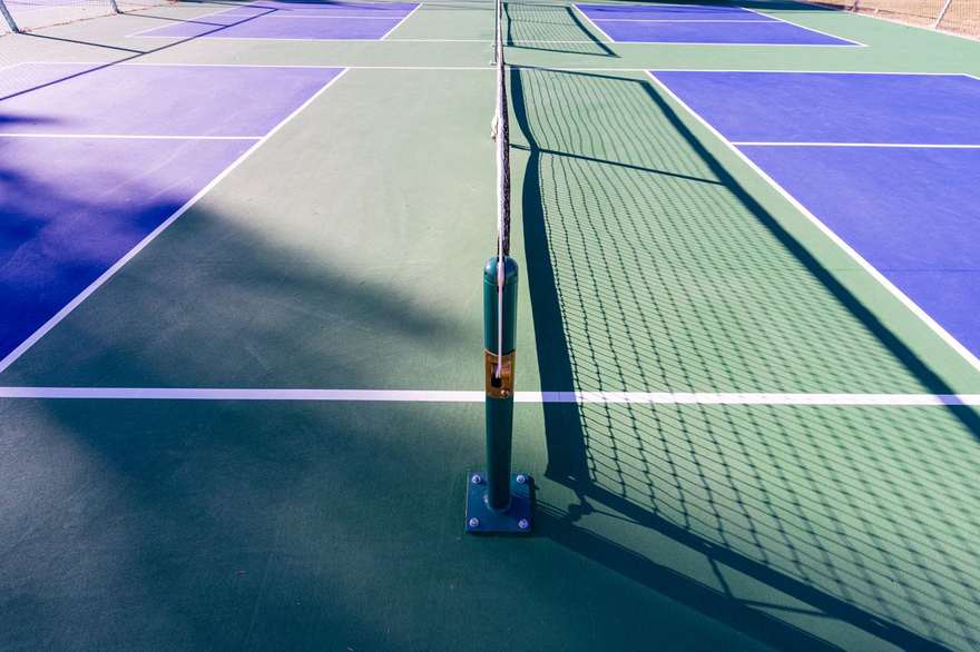 An empty outdoor pickleball court with a net in summer sun