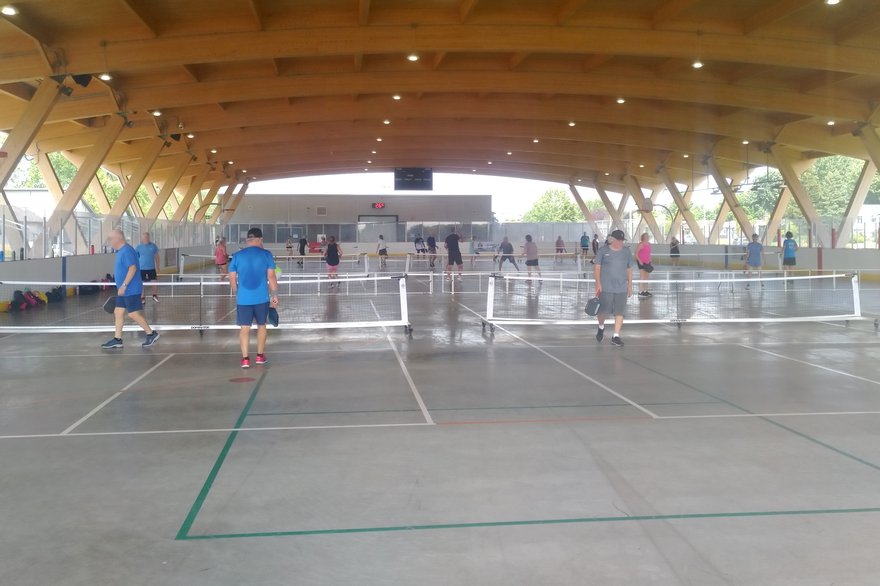 Pickleball players on covered outdoor courts during a busy open play session