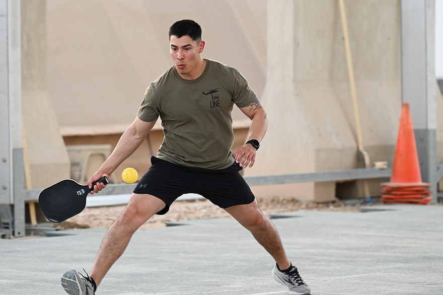 A player crouches low to retrieve a hard-hit ball during an outdoor recreational match
