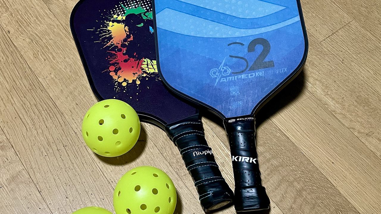Pickleballs and two paddles on a wooden surface