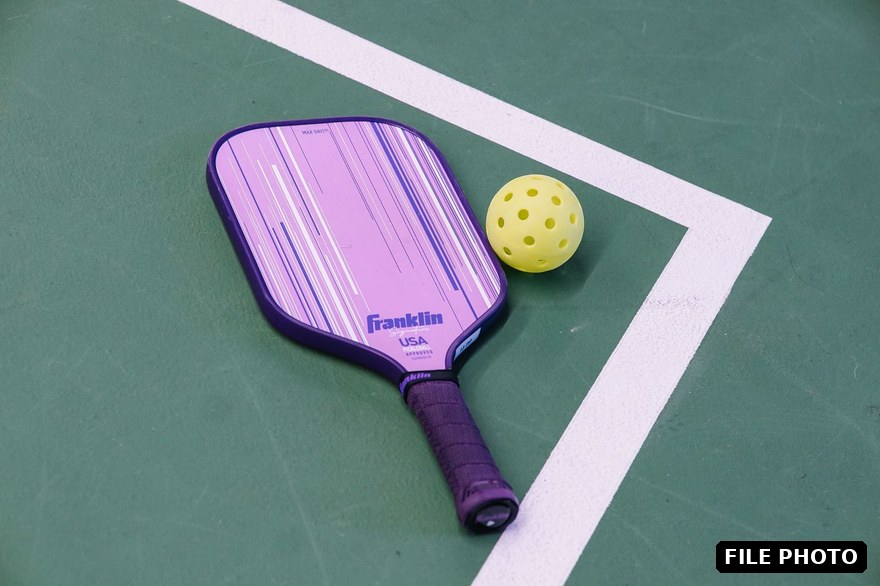 A pickleball paddle and yellow ball on the corner of a green court