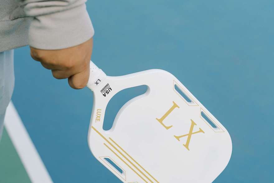 A hand holding a pickleball paddle on an outdoor court