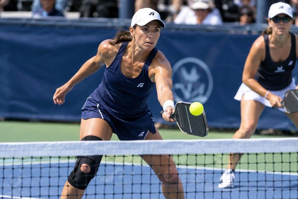 A female professional pickleball player with a supportive knee brace competing in a doubles match on an outdoor court