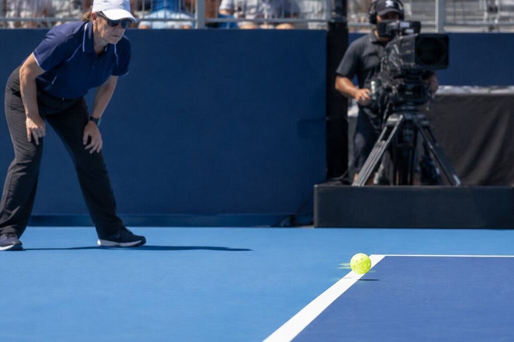 A pickleball ball landing near the sideline on a pro court with a referee watching closely