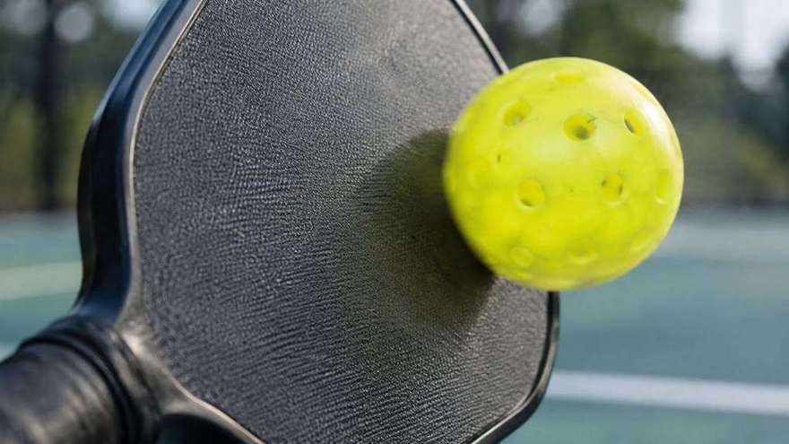Close-up of a textured pickleball paddle face with a ball in motion against it