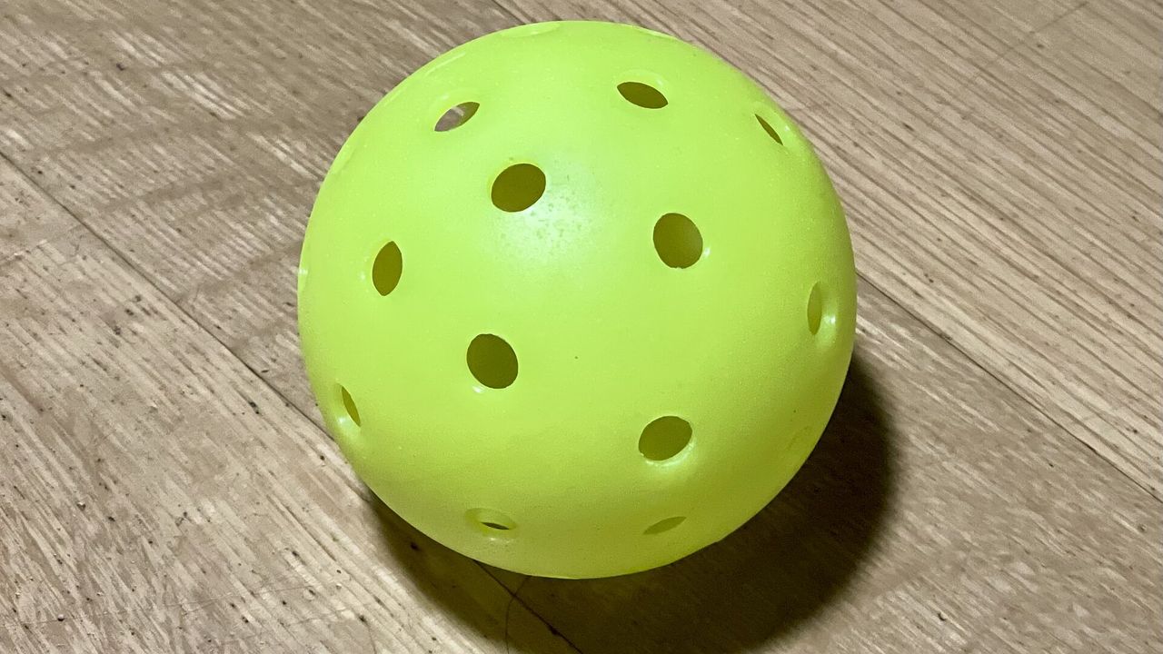 A single yellow-green perforated pickleball on a wooden surface