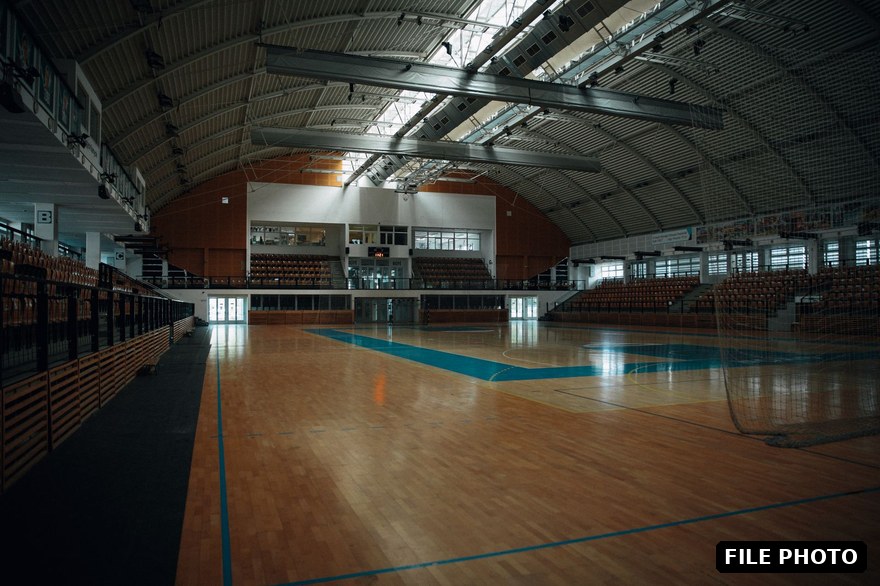 An empty indoor sports hall with a polished wooden court floor and spectator seating