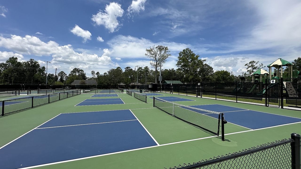 Blue and green pickleball courts with nets under a partly cloudy sky