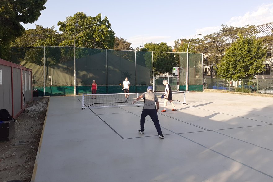 Four players in a doubles pickleball rally at an outdoor court during a club training session