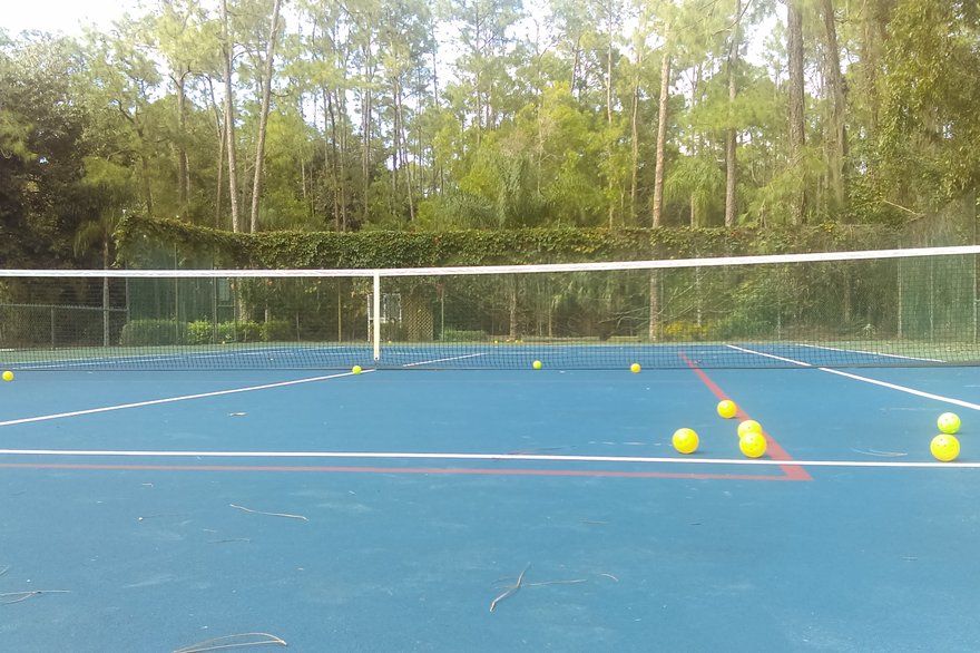 Yellow pickleballs scattered on a blue tennis court marked with red pickleball lines