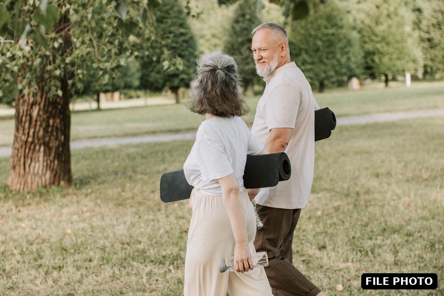 An older couple walking through a park carrying yoga mats