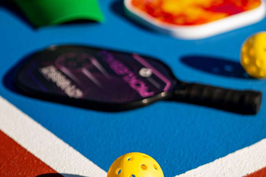 Yellow pickleballs and a paddle on a blue and orange court