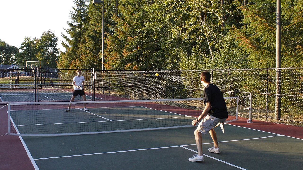 Player in a pickleball match on an outdoor court with trees behind