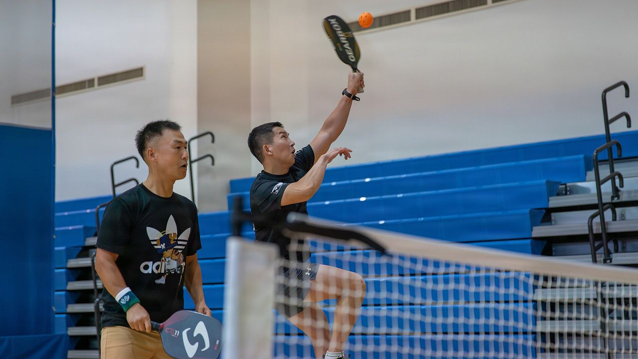 A player reaching up with a paddle at the net during a pickleball game