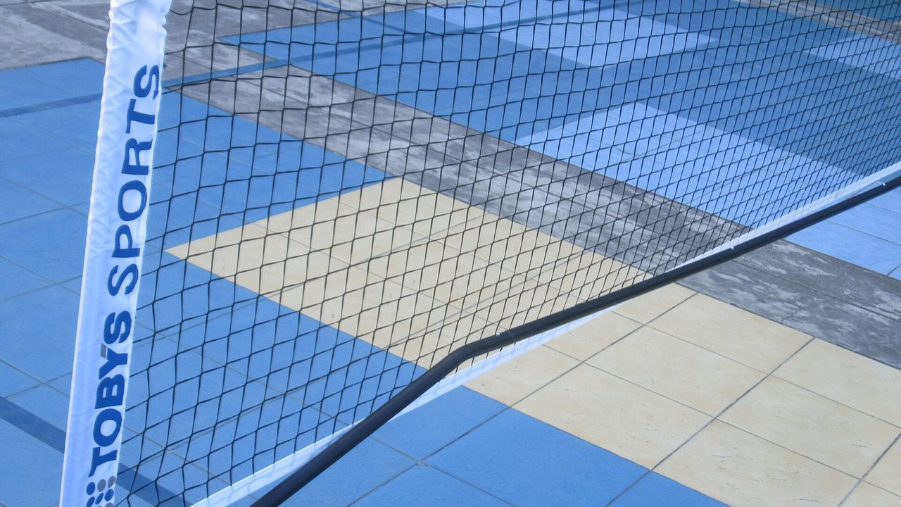 The edge of a portable pickleball net with branded tape on a court
