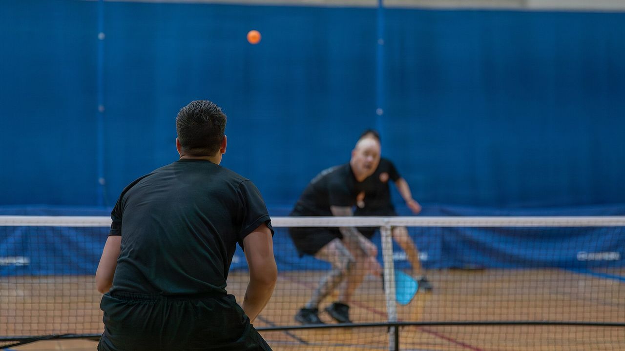 Two players in a pickleball rally at the net in a gym