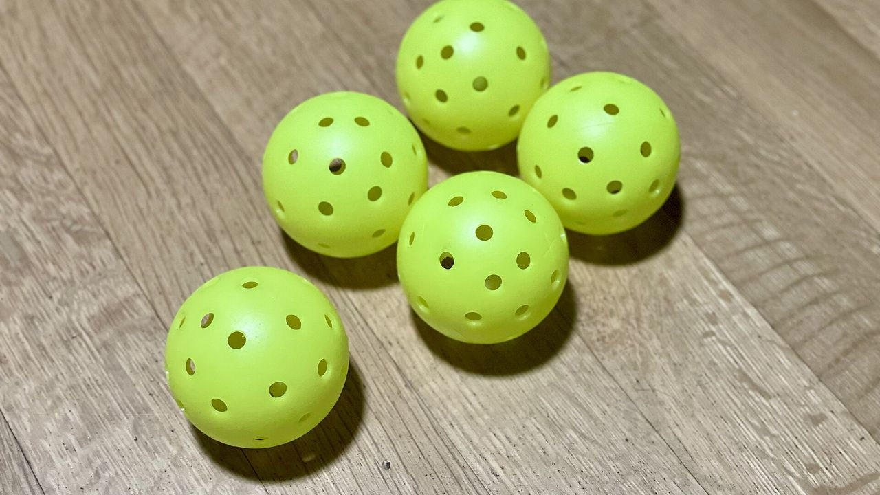 Five yellow-green pickleballs on a wooden surface