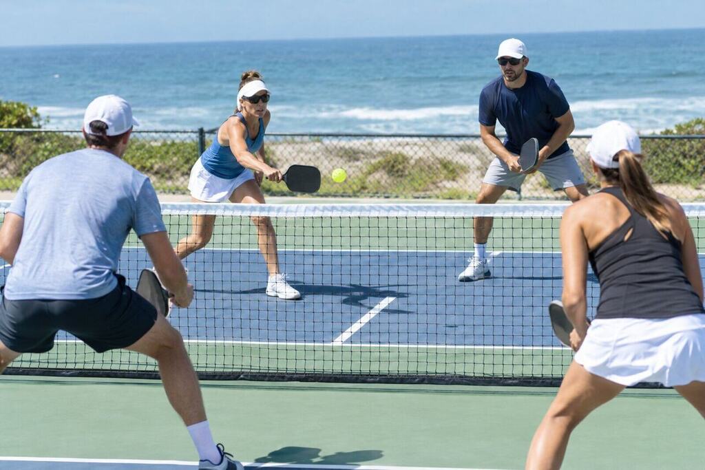 Professional pickleball doubles match in progress on an outdoor court, players spread wide at the baseline