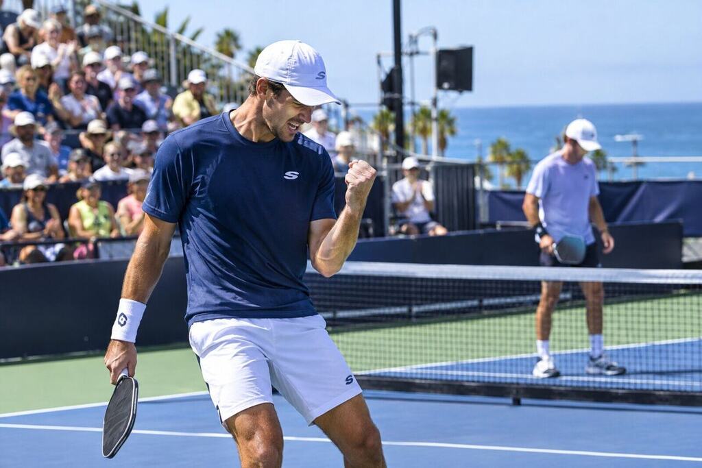 A professional pickleball player celebrating a winning point with a fist pump on an outdoor tournament court