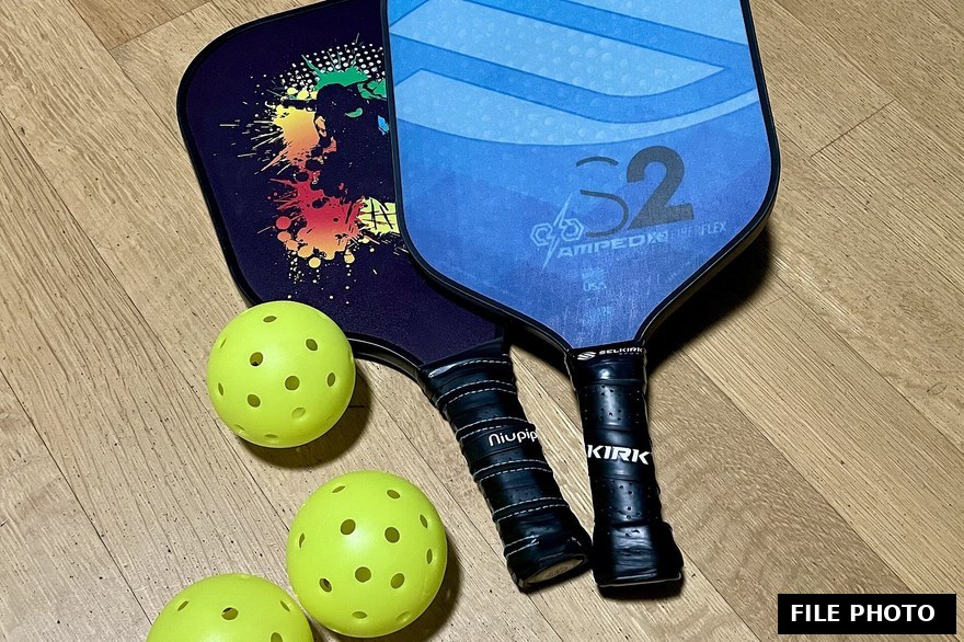 A pickleball paddle and ball resting on a court corner