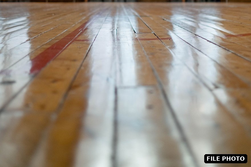 A polished wooden gymnasium floor with court lines in an empty hall