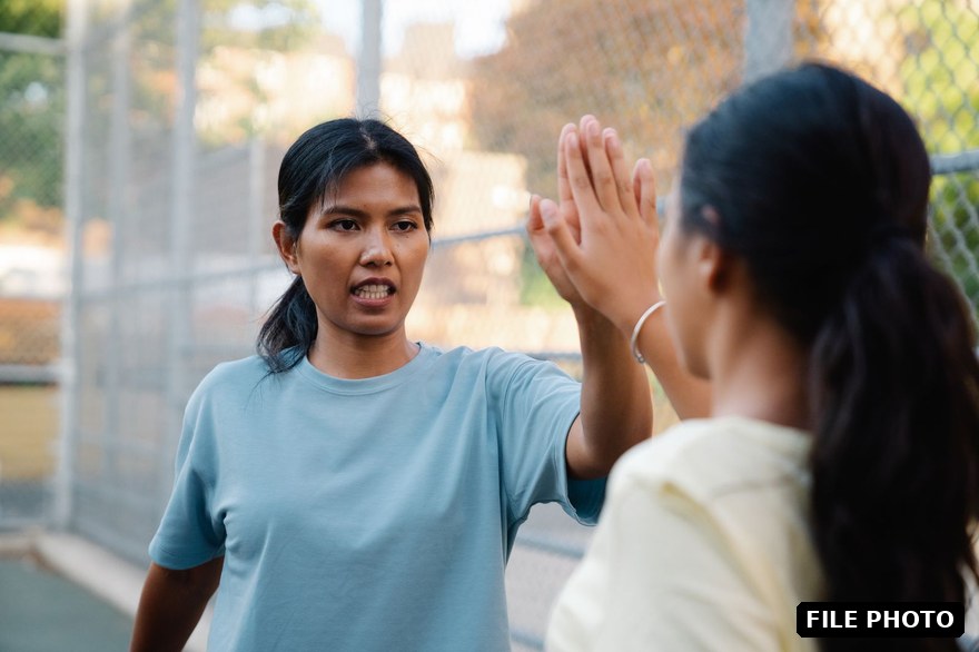Two young women high-fiving on an outdoor court after a game